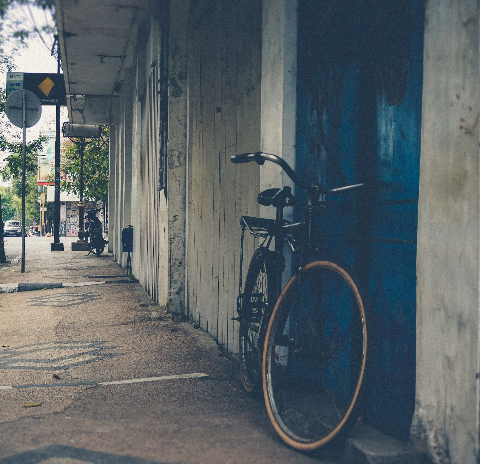 A black commuter bike parked by a blue door on a quiet street.